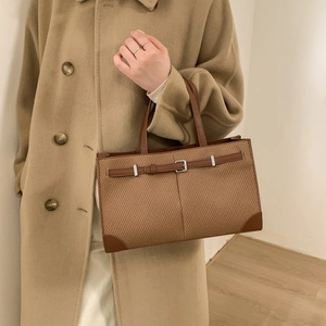 Detail of a brown woven texture tote bag with leather straps and metallic buckle detail