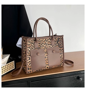 Detail of leopard print tote bag featuring two brown leather front pockets on a wooden shelf
