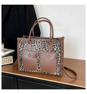 Detail of leopard print tote bag featuring brown leather pockets and reinforced handles