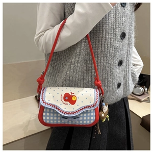 Detail of plaid crossbody bag with apple print, blue bow, and cute bear pendant