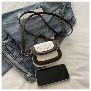 Detail of mini cherry print bag with adjustable strap next to a smartphone for scale