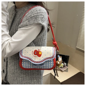 Detail view of a blue and white checkered shoulder bag with cute apple print and plush charm