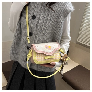 Detail of sweet pink and yellow checkered crossbody bag with cute apple motif and bear charm
