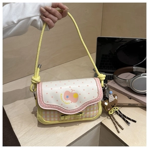 Detail of pink and yellow apple-themed handbag with cherry logo and bear charm