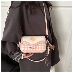 Detail of pink plaid crossbody bag with cherry patterns and decorative plush charm