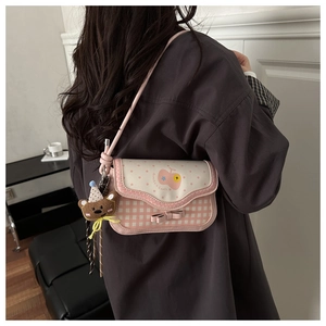 Detail of pink plaid crossbody bag with bow accent and cute bear plush charm on strap