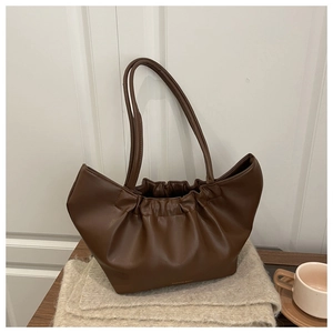 Close-up of brown pleated cloud tote bag with thin strap on a rustic wooden table