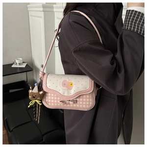 Detail of pink plaid saddle bag with cute bear charm and bow decoration on the flap