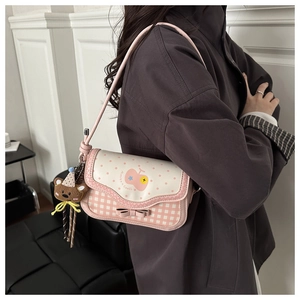 Detail of pink plaid crossbody bag with cherry print, bow accent, and cute bear charm