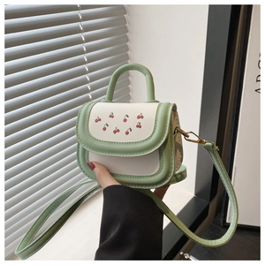 Detail of mini green and white handbag featuring cherry patterns and gold hardware