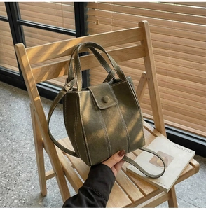 Close-up of olive green vintage bucket bag on wooden chair with natural sunlight shadows