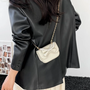Cream mini crossbody bag with bow and pearls on a model wearing black leather blazer