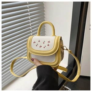 Detail of yellow and white crossbody bag with red cherry print and slender shoulder strap