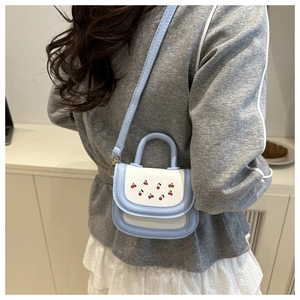 Mini cherry print bag with blue trim and white flap shown on a model cross-body style