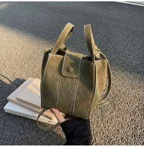 Detail of dark green suede bucket bag with magnetic flap and contrast white stitching