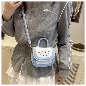 Model wearing a mini light blue and white crossbody bag with cute red cherry prints