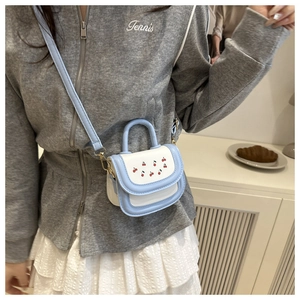 Detail of a mini cherry print crossbody bag with blue and white color-block and gold hardware
