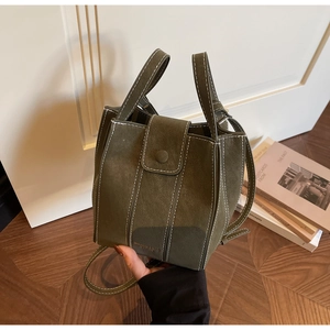 Detailed view of dark green suede bucket bag with white contrast stitching and dual handles