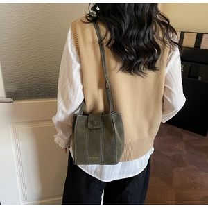 Detail of dark green leather bucket bag with vertical white stitching and gold brand logo