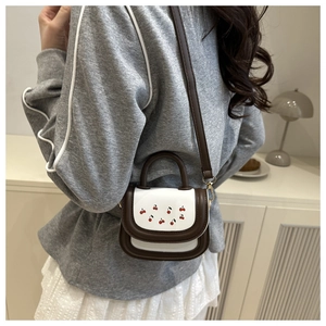Detail of a mini crossbody bag with cherry embroidery and brown and white contrast leather