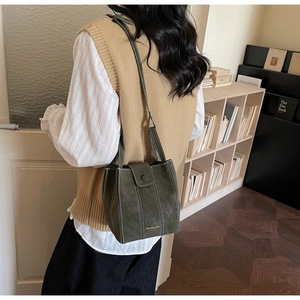 Detail of dark green leather bucket bag featuring white contrast stitching and magnetic flap