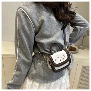 Mini white leather saddle bag with cherry print and brown trim on a casual model