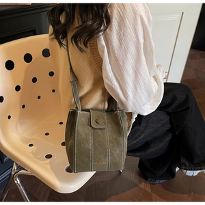 Detail of dark green suede bucket bag with white contrast stitching and gold logo