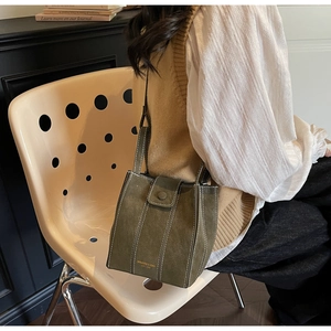 Detail view of dark green suede bucket bag featuring white contrast stitching and gold logo