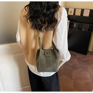 Detail of olive green suede bucket bag featuring contrast white stitching and gold logo