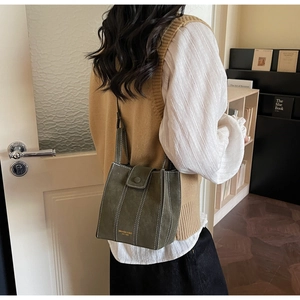 Detail of dark green crossbody bag with white stitching and gold logo on leather