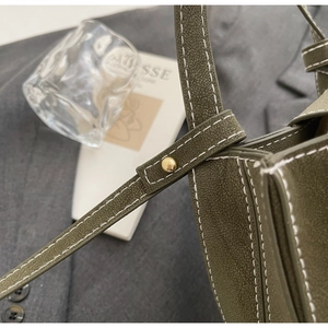Detailed close-up of a green faux leather bucket bag with white stitching and gold rivets