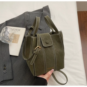Detailed shot of dark green bucket bag with white stitching and brand gold logo