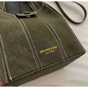 Detail view of olive green retro bucket bag featuring white stitching and gold lettering