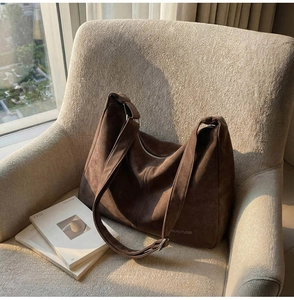 Borsa hobo grande in pelle marrone scuro posata su una poltrona in tessuto beige