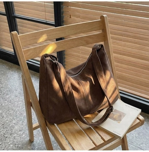 Dettaglio borsa tote in pelle scamosciata marrone scuro con cerniera su sedia di legno