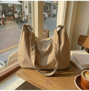 Primo piano di borsa hobo in pelle scamosciata cammello con tracolla larga sul tavolo