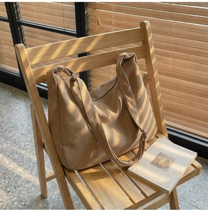 Dettaglio della grande borsa hobo in finto scamosciato color cammello su una sedia di legno