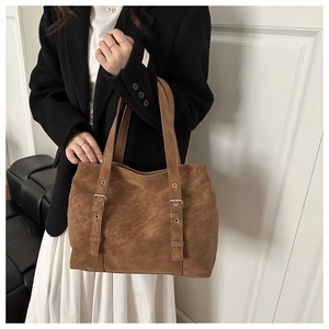 Brown suede tote bag with decorative straps and silver buckles worn by a model