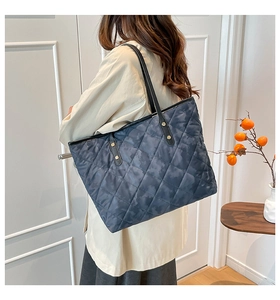 Detail of grey quilted tote bag with diamond pattern and black shoulder straps