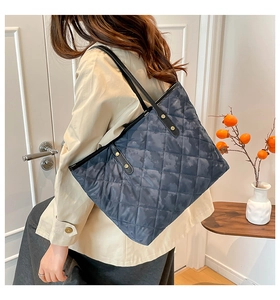 Close-up of a large quilted navy blue tote bag with durable leather shoulder straps