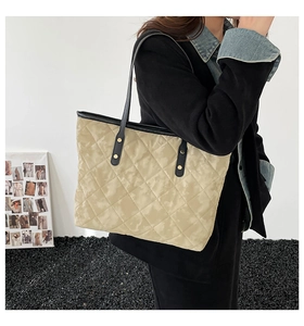 Detailed side view of beige quilted tote bag with black straps and golden rivets