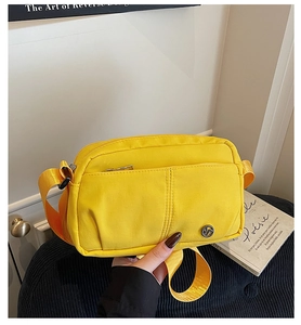 Detail view of a yellow nylon crossbody square bag with a front zip pocket and logo