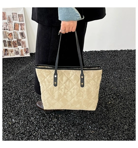 Close-up of beige quilted tote bag with diamond stitching and black straps detail
