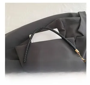 Detail of woven leather handle with gold metal hooks on a black minimalist shoulder bag