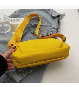Detail of soft yellow nylon crossbody bag with wide shoulder strap and metal logo