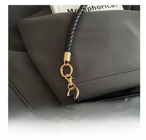 Detail of ruched black leather bag showing golden metal hook and braided shoulder strap