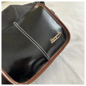 Gros plan du sac en similicuir brillant noir avec bordure brune et logo doré