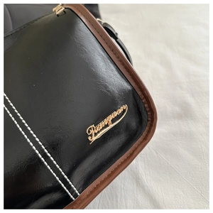 Détail d'un sac bandoulière en cuir noir avec bord brun, coutures et logo doré