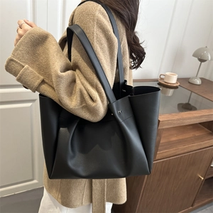 Classic black matte leather tote bag with long straps worn on shoulder by model
