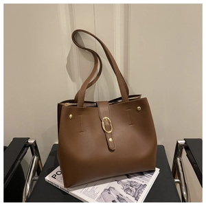 Detail of a brown leather tote bag with gold oval buckle and zipper on a magazine